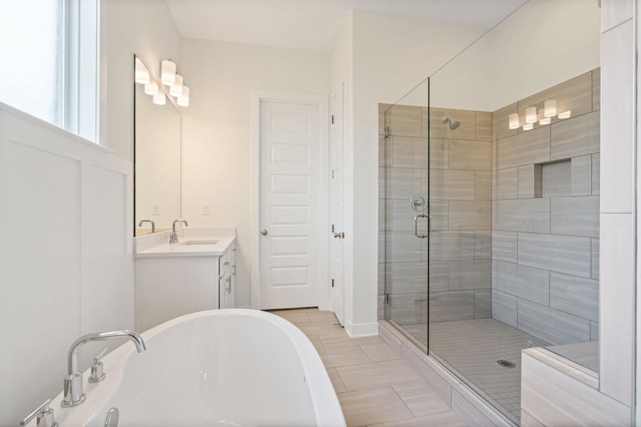 Bathroom featuring a freestanding soaking tub with chrome fixtures, a walk-in shower with glass enclosure and tiled walls, a single vanity with a white countertop, and light wood-finish flooring Bathroom featuring a freestanding soaking tub with chrome fixtures, a walk-in shower with glass enclosure and tiled walls, a single vanity with a white countertop, and light wood-finish flooring