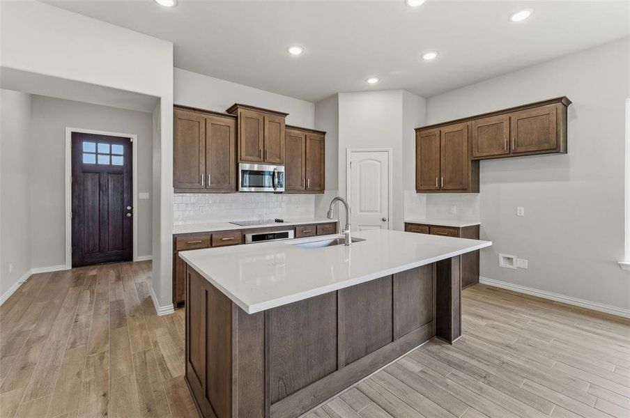 Kitchen featuring an island with sink, light wood-style floors, light stone countertops, stainless steel microwave, and recessed lighting