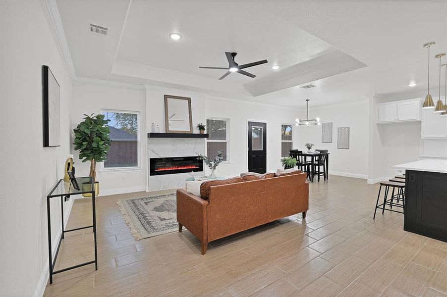 Living room featuring a raised ceiling, a fireplace, ceiling fan with notable chandelier, and light hardwood / wood-style flooring