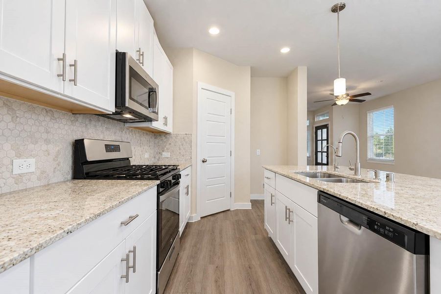 Stylish kitchen features white cabinetry, stone countertops, stainless steel appliances, a decorative tile backsplash, and a spacious center island with double sink and dishwasher. Pendant lighting adds a polished finishing touch, while the open layout keeps the kitchen connected to the surrounding living spaces. Stylish kitchen features white cabinetry, stone countertops, stainless steel appliances, a decorative tile backsplash, and a spacious center island with double sink and dishwasher. Pendant lighting adds a polished finishing touch, while the open layout keeps the kitchen connected to the surrounding living spaces.