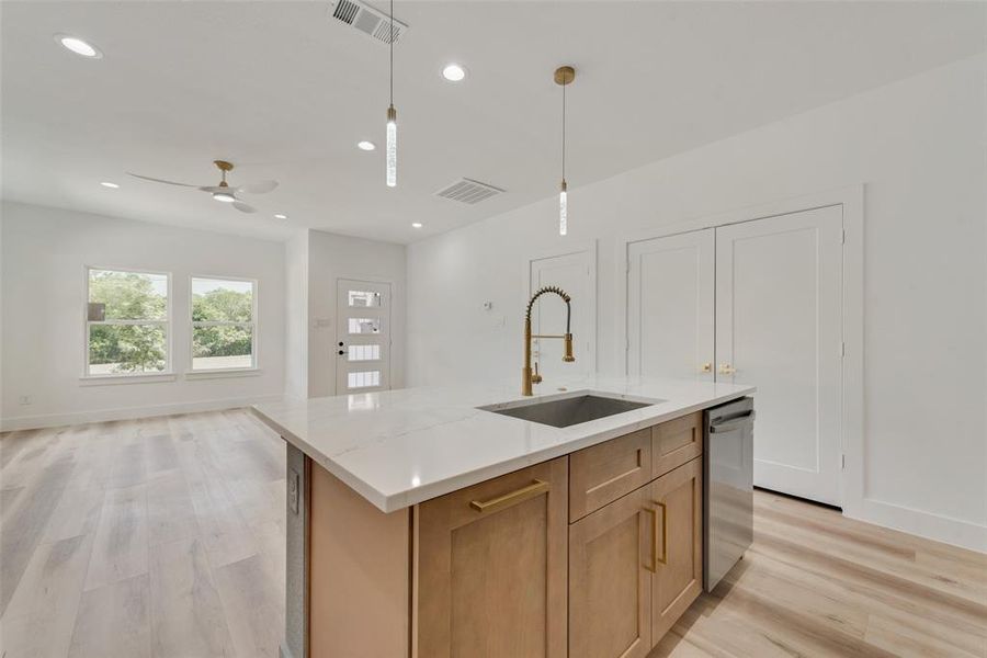 Kitchen featuring ceiling fan, light wood-type flooring, pendant lighting, sink, and a center island with sink