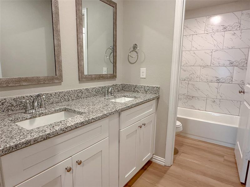 Full bathroom with toilet, hardwood / wood-style floors, tiled shower / bath combo, and double sink vanity