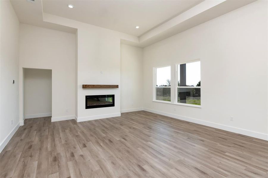 Unfurnished living room with recessed lighting, light wood-type flooring, baseboards, a high ceiling, and a glass covered fireplace