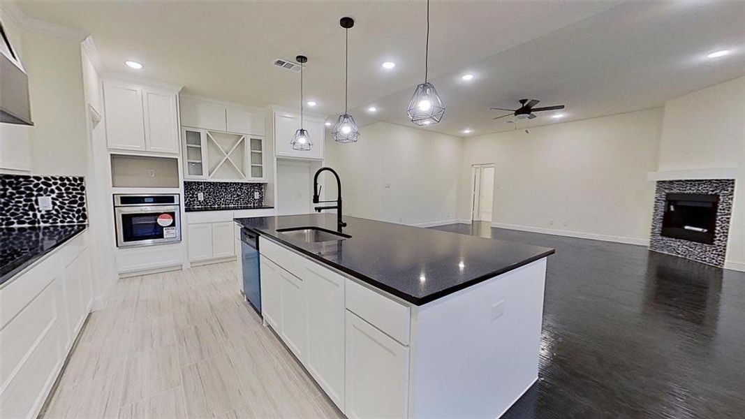 Kitchen with a center island with sink, a fireplace, tasteful backsplash, white cabinets, and stainless steel appliances Kitchen with a center island with sink, a fireplace, tasteful backsplash, white cabinets, and stainless steel appliances