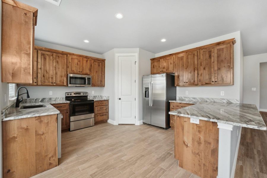 Kitchen with light stone counters, a peninsula, stainless steel appliances, and a sink