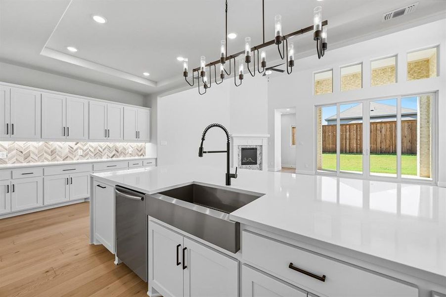 Kitchen featuring white cabinetry, decorative backsplash, a premium fireplace, light wood-type flooring, and stainless steel dishwasher