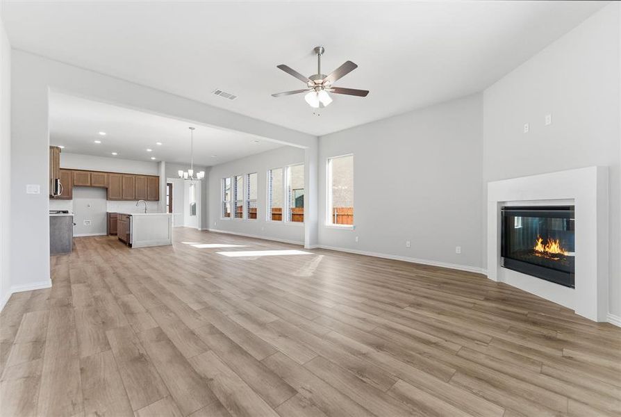 Unfurnished living room featuring a chandelier, a glass covered fireplace, light wood-style flooring, a ceiling fan, and recessed lighting