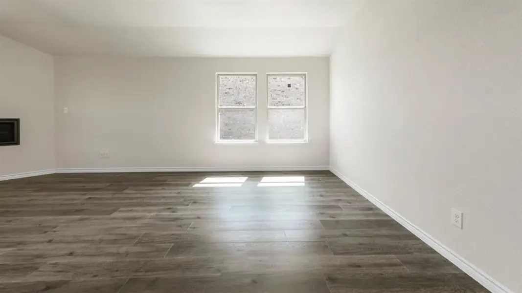 Spacious room featuring wood-finish flooring, white baseboards, and two windows