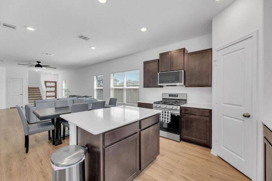 Kitchen featuring light wood-style floors, visible vents, appliances with stainless steel finishes, and dark brown cabinetry