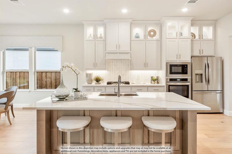 Kitchen with large island, white cabinets, quartz countertops, and stainless steel appliances including refrigerator and wall oven.