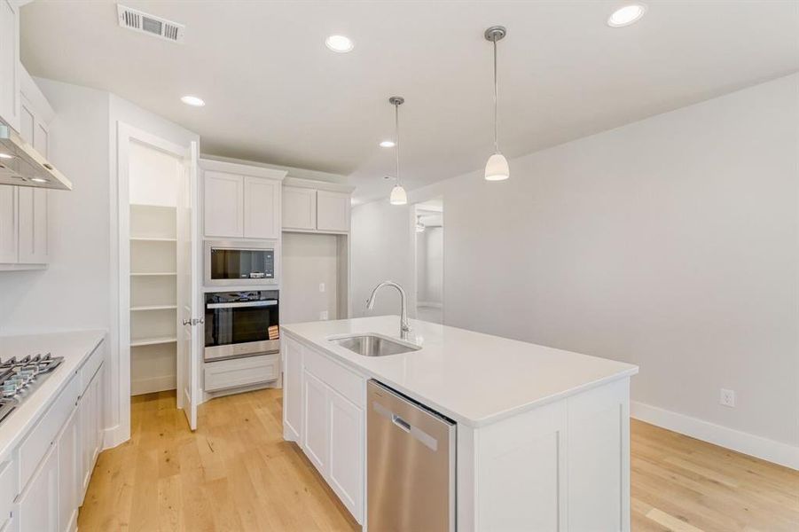 Kitchen with a kitchen island with sink, stainless steel appliances, white cabinetry, and light wood finished floors