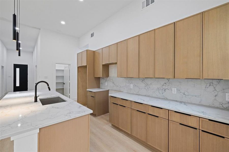 Kitchen with light stone countertops, light brown cabinets, a kitchen island with sink, modern cabinets, and recessed lighting