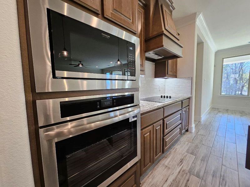Kitchen with built in microwave, stainless steel oven, ornamental molding, premium range hood, and tasteful backsplash