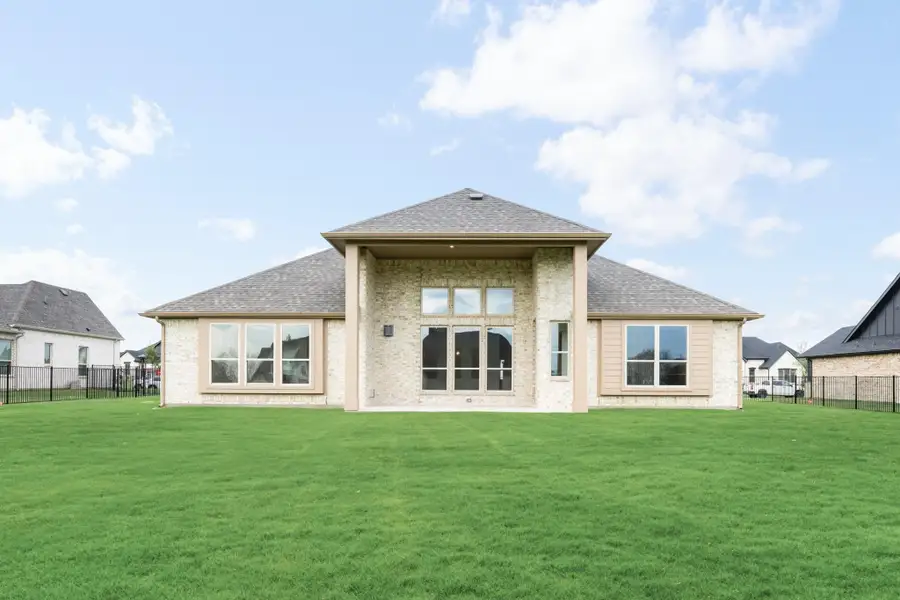 Rear exterior of single-story home with light brick, hip roof, large windows, and spacious fenced backyard lawn. Rear exterior of single-story home with light brick, hip roof, large windows, and spacious fenced backyard lawn.