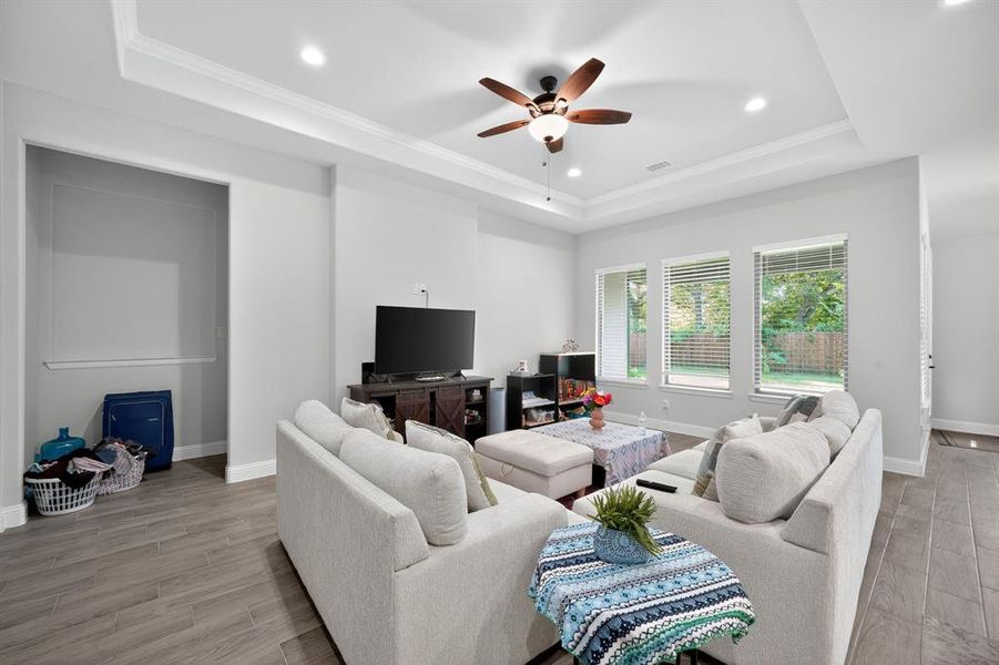 Living room featuring a tray ceiling, recessed lighting, light wood-type flooring, ceiling fan, and crown molding