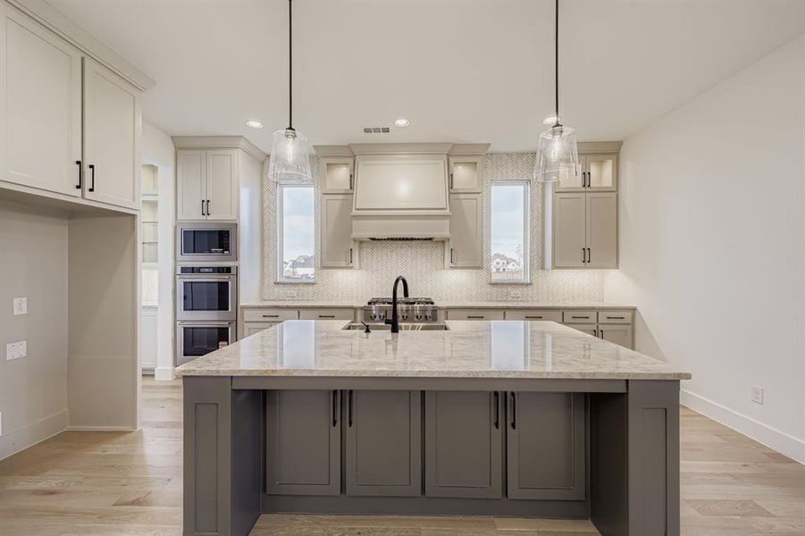 Kitchen featuring light stone counters, hanging light fixtures, an island with sink, white cabinets, and light wood-style floors