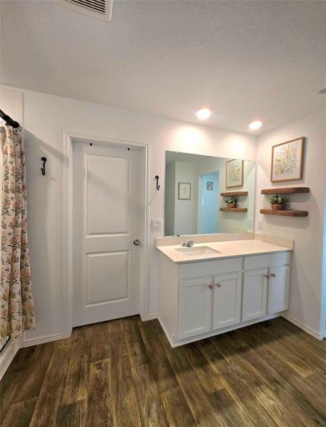 Bathroom vanity featuring white cabinetry with brushed nickel hardware, a white countertop with an integrated sink, and an expansive wall-mounted mirror