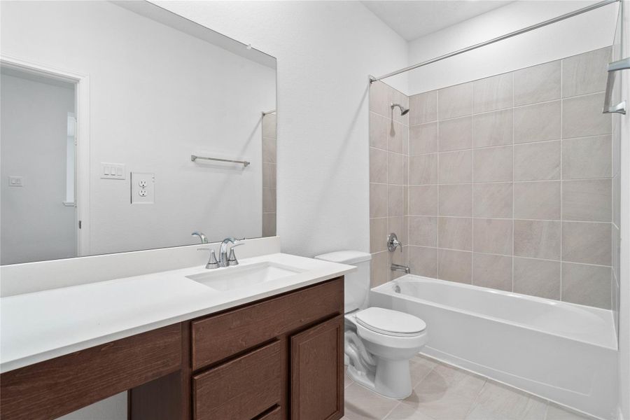 The secondary bathroom showcases tile flooring, a bath/shower combo with Daltile tile surround, vanity with knee space and a stunning light countertop, a stylish mirror, sleek fixtures, and contemporary finishes throughout.