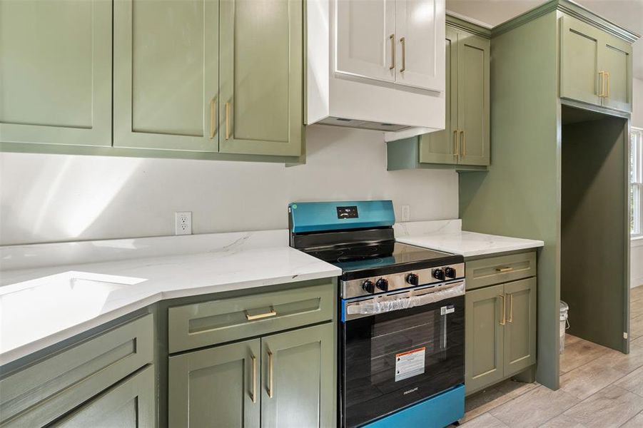 Kitchen featuring sage green cabinetry, white upper cabinets, light-toned countertops, and a modern range oven with a blue finish Kitchen featuring sage green cabinetry, white upper cabinets, light-toned countertops, and a modern range oven with a blue finish