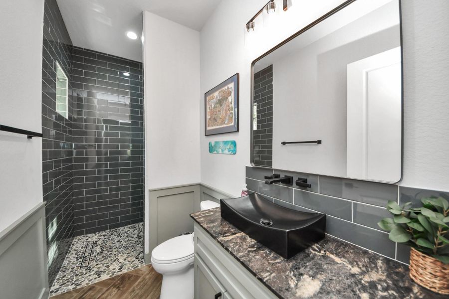 Elegant bathroom featuring a sleek black vessel sink and modern fixtures, complemented by a stylish glass-tiled shower and stone flooring for a touch of luxury.