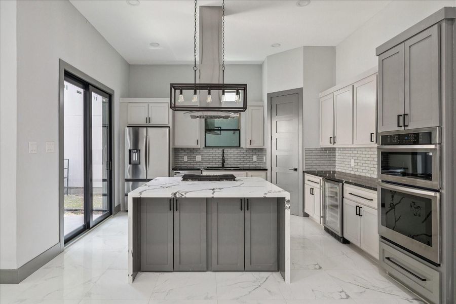 From this view, the island serves as the central hub, perfectly positioned for gathering while still leaving plenty of room for movement around the perimeter. The cabinetry and appliances line the back wall in an efficient arrangement, keeping everything within reach without interrupting the sightlines to the rest of the home