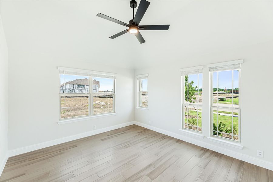 Empty room with vaulted ceiling, black ceiling fan, multiple windows, and light wood-look floors