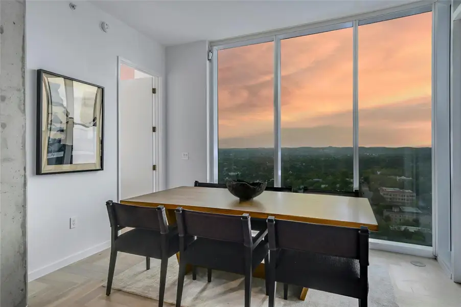 Dine with a view—this elegant dining area is set against a backdrop of expansive floor-to-ceiling windows, offering breathtaking sunset vistas over the Texas Hill Country. The sleek, modern design and warm wood tones create an inviting ambiance for intimate dinners or lively gatherings  (Photo from previous model Residence No. 2104 on lower level)