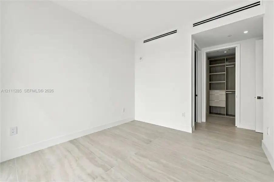 Neutral-toned tile flooring, built-in wooden closet system with shelving and drawers, and recessed linear ceiling detailing Neutral-toned tile flooring, built-in wooden closet system with shelving and drawers, and recessed linear ceiling detailing