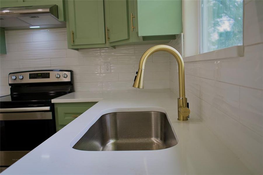Kitchen featuring green cabinetry, stainless steel range with electric stovetop, backsplash, under cabinet range hood, and light stone countertops