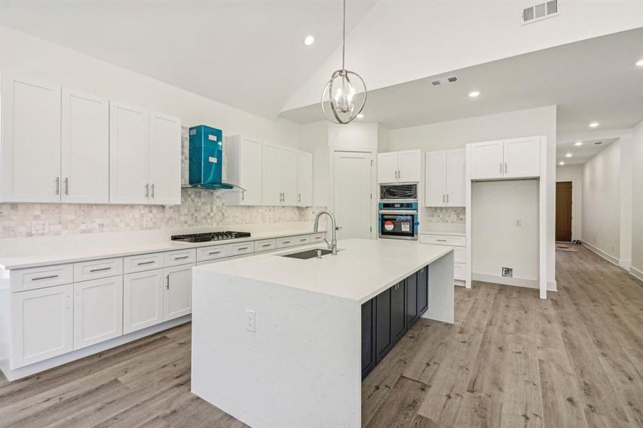 Kitchen featuring white cabinets, decorative backsplash, hanging light fixtures, wall chimney exhaust hood, and light wood-style flooring