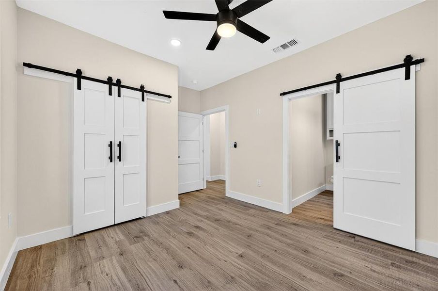 Unfurnished bedroom with a barn door, light wood-style floors, ceiling fan, a closet, and recessed lighting