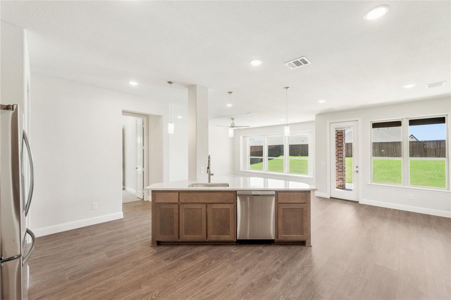 Open kitchen with center island, stainless steel appliances, and hardwood floors overlooking a bright living area