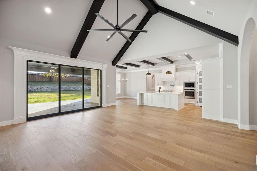 Unfurnished living room featuring ceiling fan with notable chandelier, sink, beam ceiling, light hardwood / wood-style flooring, and high vaulted ceiling