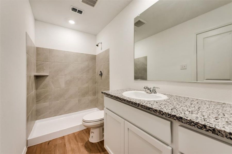 Bathroom with hardwood / wood-style floors, vanity, tiled shower, and toilet