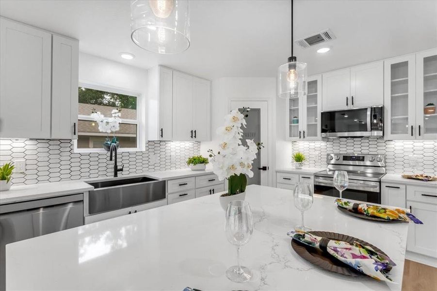 Kitchen with sink, hanging light fixtures, decorative backsplash, stainless steel appliances, and white cabinets