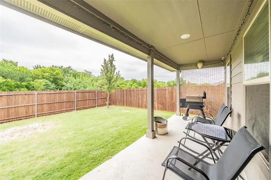 Covered outdoor patio with concrete flooring, recessed lighting, and a privacy fence enclosing the grassy yard