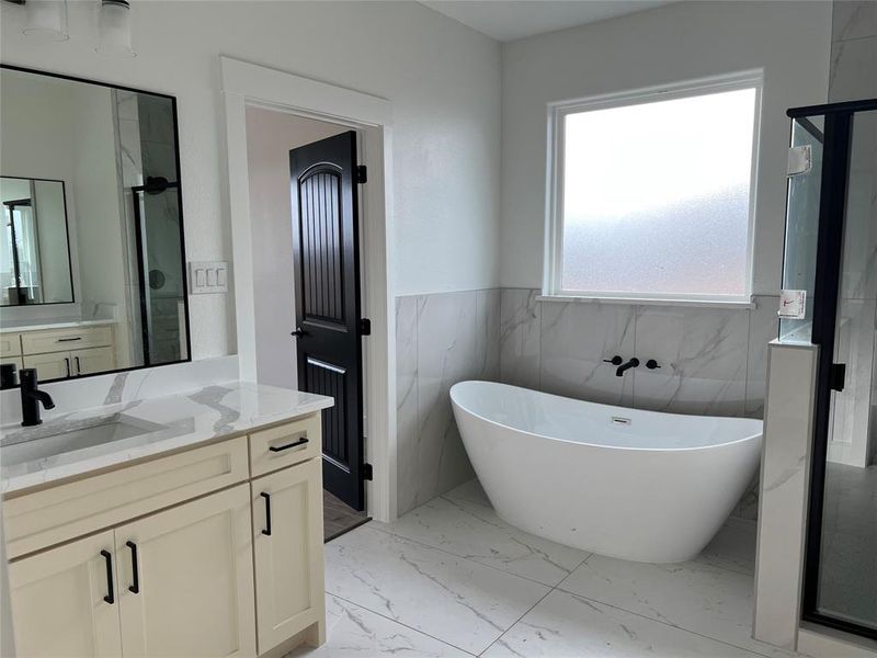 Bathroom featuring a wainscoted wall, tile walls, light marble finish flooring, a soaking tub, and a marble finish shower