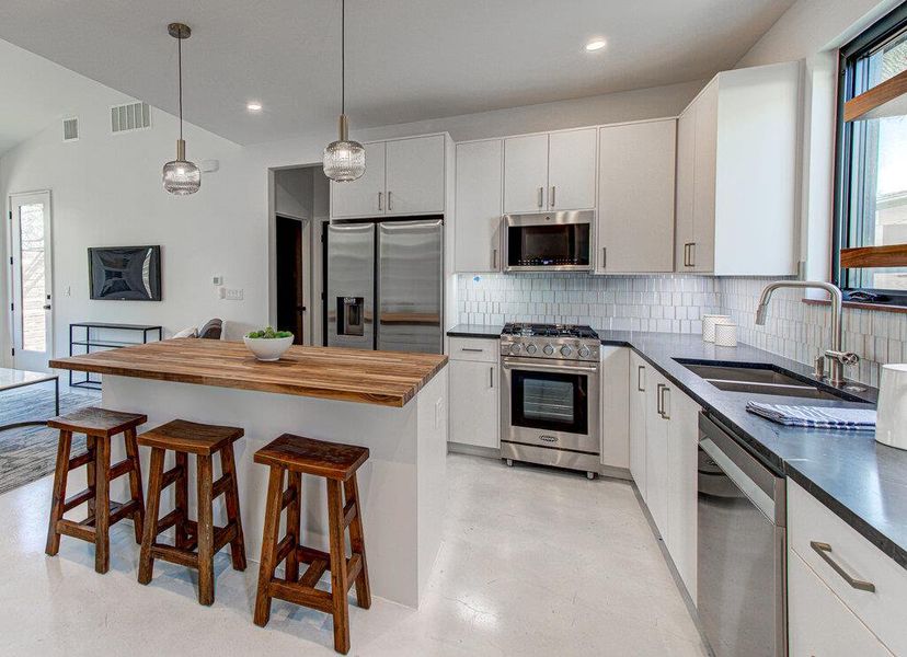 Kitchen with a breakfast bar, visible vents, decorative backsplash, appliances with stainless steel finishes, and a sink