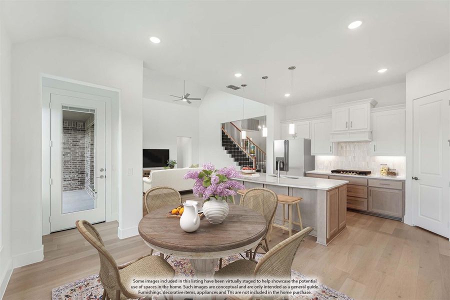 Open-plan dining area with round wood table flowing into kitchen with white cabinets and island, hardwood floors throughout