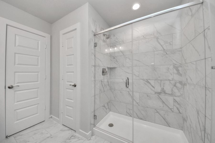 Secondary bath features tile flooring, walk-in shower with tile surround, light stained wood cabinets, beautiful light countertop.