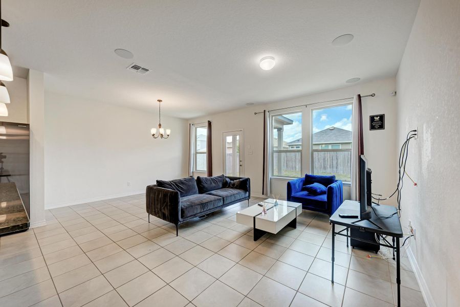 A well-lit living area features tiled flooring and ample natural light from large windows.
