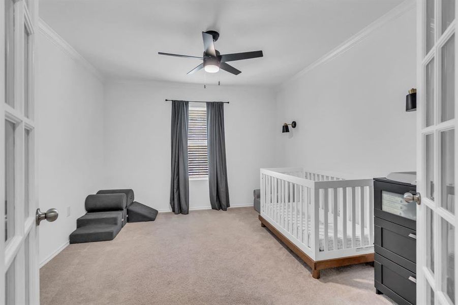 Bedroom featuring a nursery area, light carpet, ornamental molding, a ceiling fan, and french doors