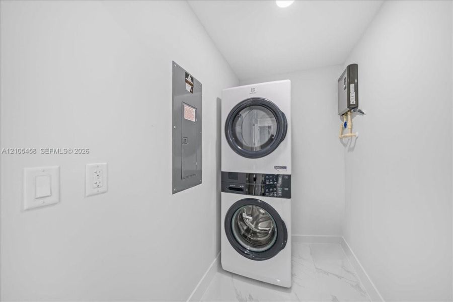 Stacked laundry appliances with a front-loading washer and dryer, recessed lighting, and large format floor tiling Stacked laundry appliances with a front-loading washer and dryer, recessed lighting, and large format floor tiling