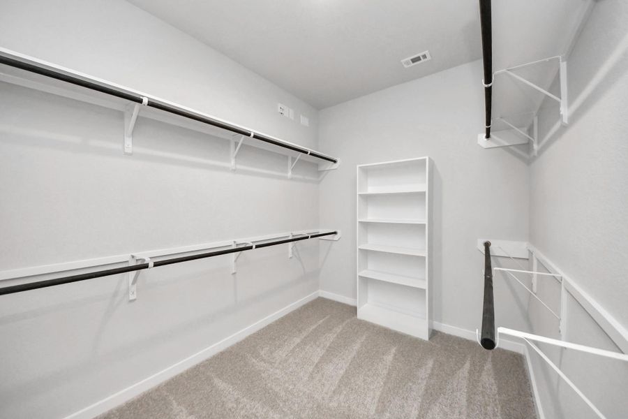 Walk-in closet that epitomizes luxury and practicality. This generously sized space features built-in shelving, offering abundant room for impeccable organization. High ceilings and recessed lighting create a bright and welcoming ambiance. Sample photo of completed home with similar floor plan. Actual colors and selections may vary.