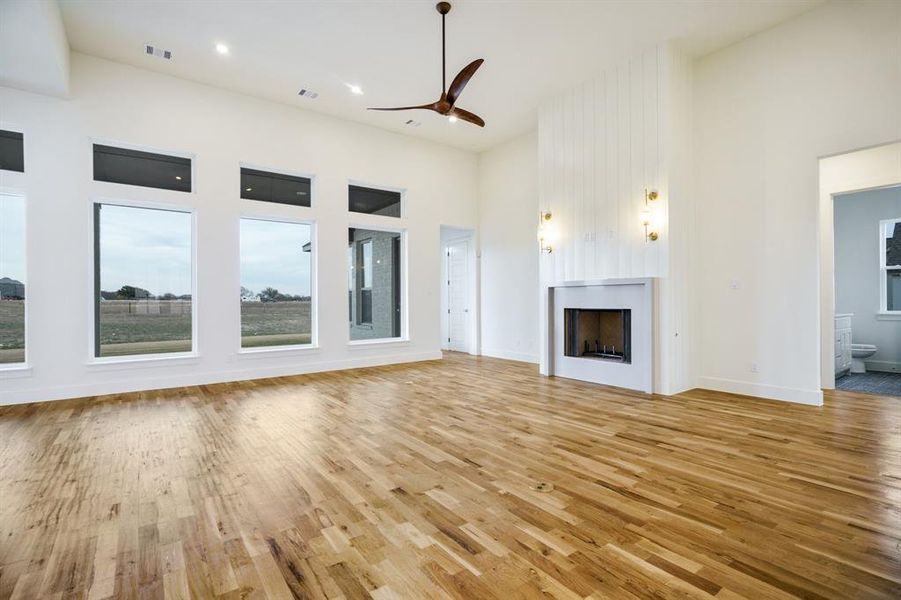 Unfurnished living room featuring ceiling fan, light wood-type flooring, and a towering ceiling