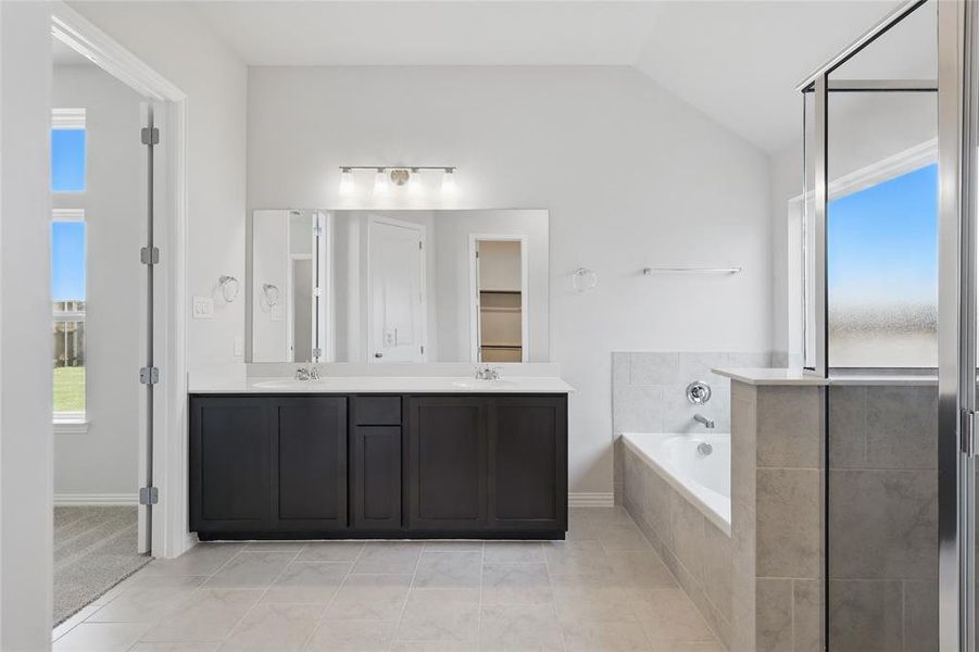 Full bath featuring a garden tub, double vanity, lofted ceiling, tile patterned flooring, and baseboards