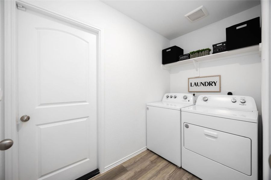 This photo showcases a clean, compact laundry room featuring a washer and dryer with a shelf above for storage.