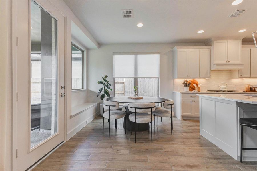 Bright, modern kitchen and dining area. It features light cabinetry, a round dining table with stylish chairs, and large windows that let in plenty of natural light. The space has a clean, contemporary feel with wood-look flooring and a view to an outdoor area through a glass door. Bright, modern kitchen and dining area. It features light cabinetry, a round dining table with stylish chairs, and large windows that let in plenty of natural light. The space has a clean, contemporary feel with wood-look flooring and a view to an outdoor area through a glass door.