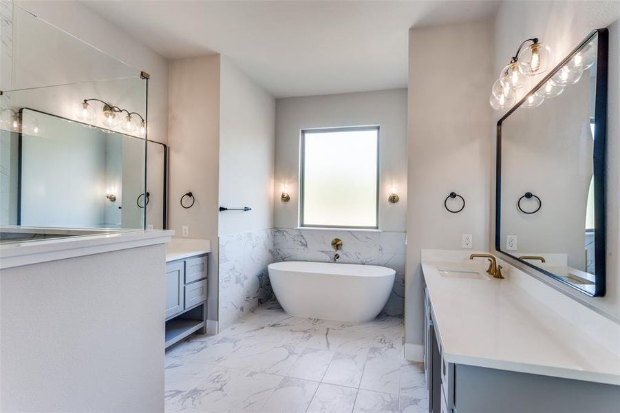 Bathroom with tile walls, a soaking tub, two vanities, wainscoting, and light marble finish floors Bathroom with tile walls, a soaking tub, two vanities, wainscoting, and light marble finish floors