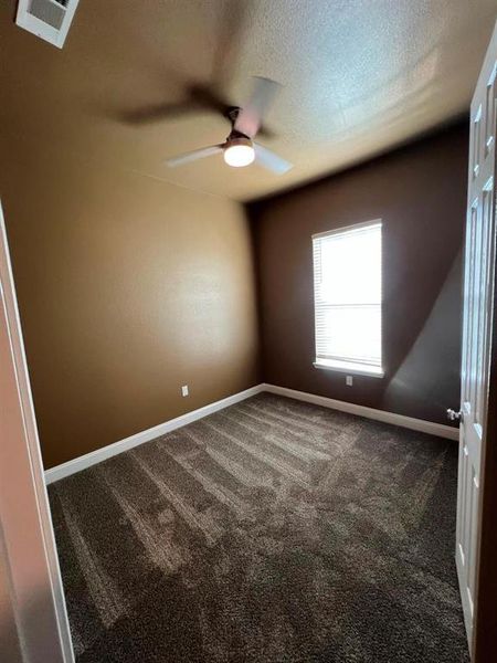 Empty room featuring dark carpet, a textured ceiling, and a ceiling fan Empty room featuring dark carpet, a textured ceiling, and a ceiling fan
